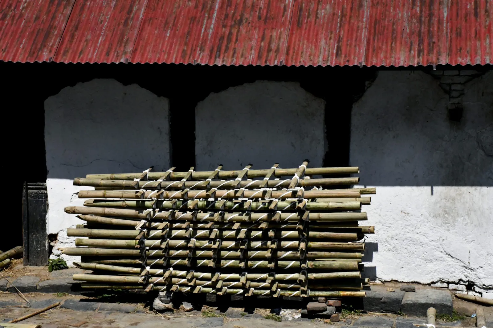 A stack of cut bamboo culms tied in a lattice and drying against a whitewashed wall